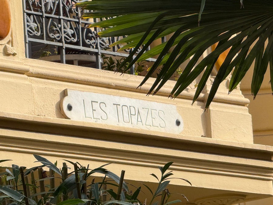 Lettres sculptées « Les Topazes » au-dessus d’une porte, entre des palmes