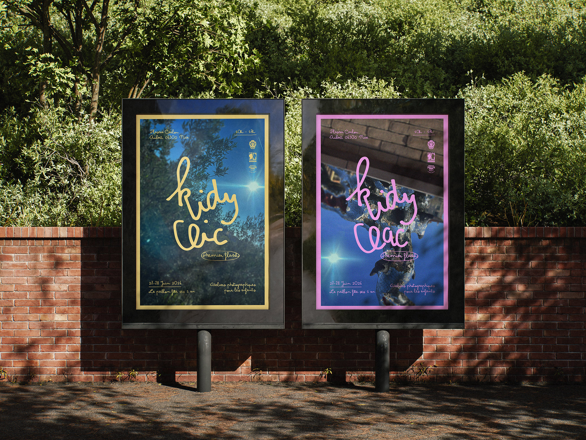 Les deux affiches Kidy Clic et Kidy Clac côte à côte sur des panneaux, devant un mur de briques et de la verdure