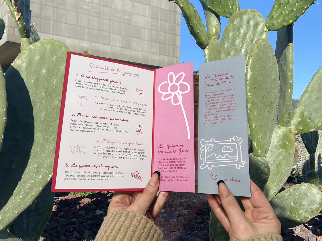 Le dépliant ouvert devant des cactus : le programme, une fleur et des dessins roses