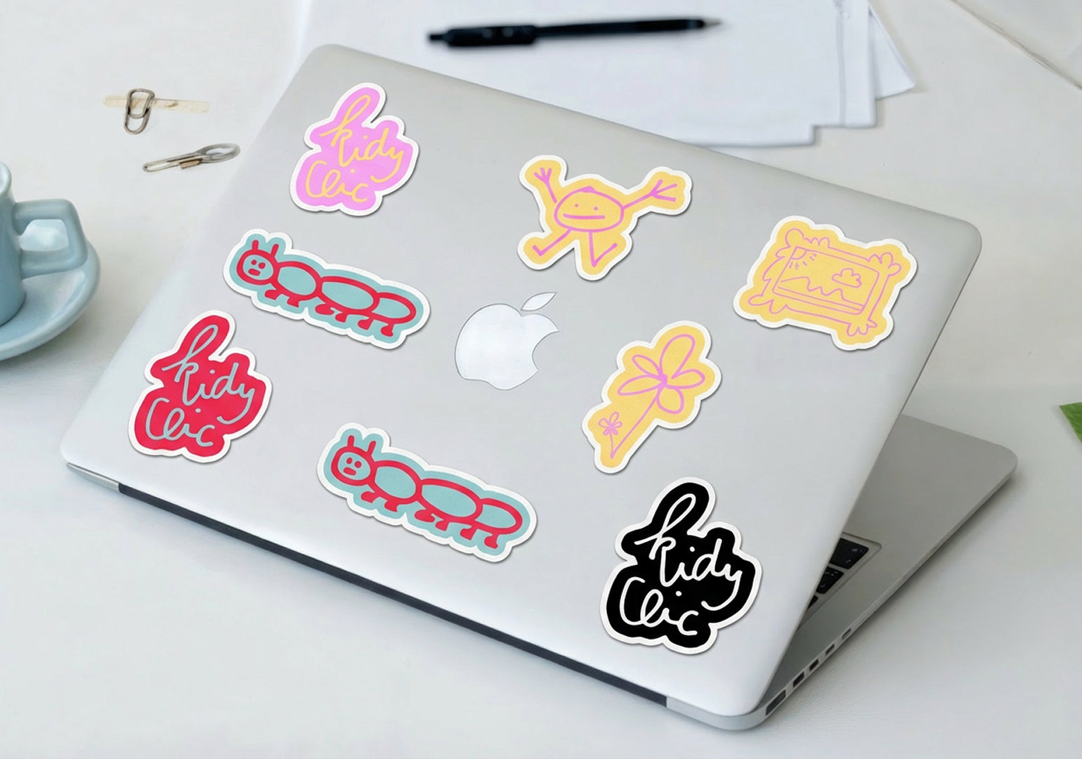 Des autocollants Kidy Clic collés sur un ordinateur portable : le logo, une chenille, un bonhomme, une fleur, un tableau