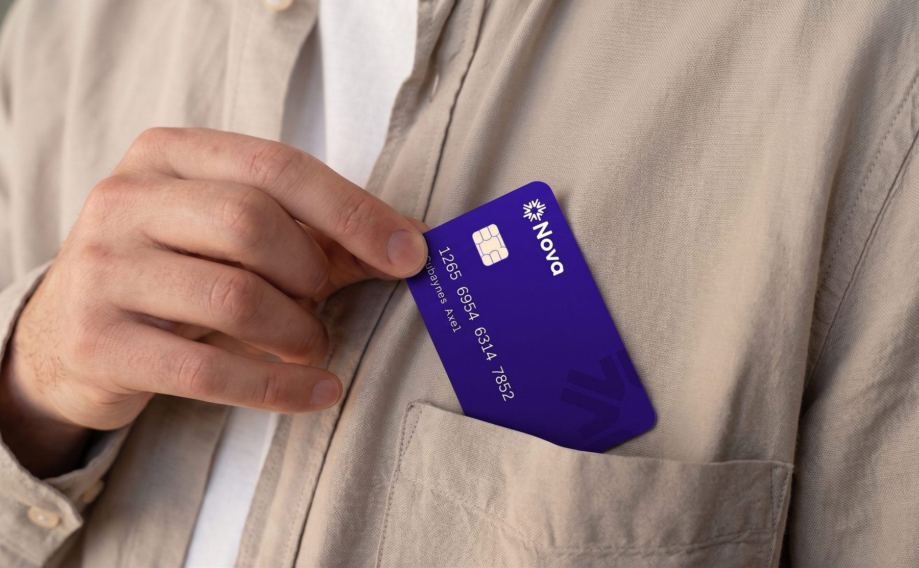 Une main glisse la carte bancaire Nova, violette, dans la poche d’une chemise en lin