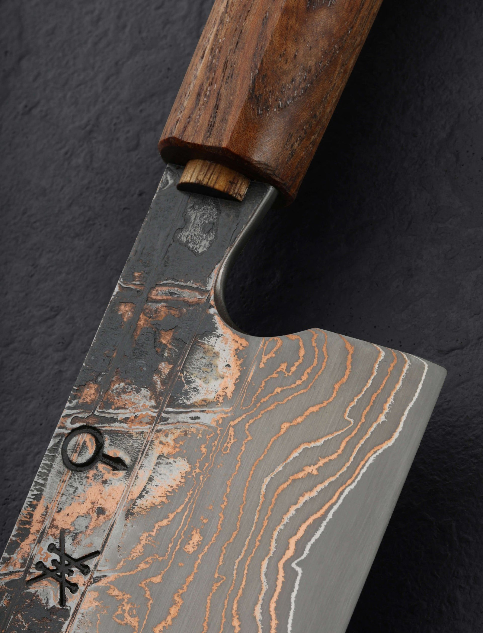 Un couteau d'Echizen en gros plan : lame damassée aux veines cuivrées, virole et manche en bois