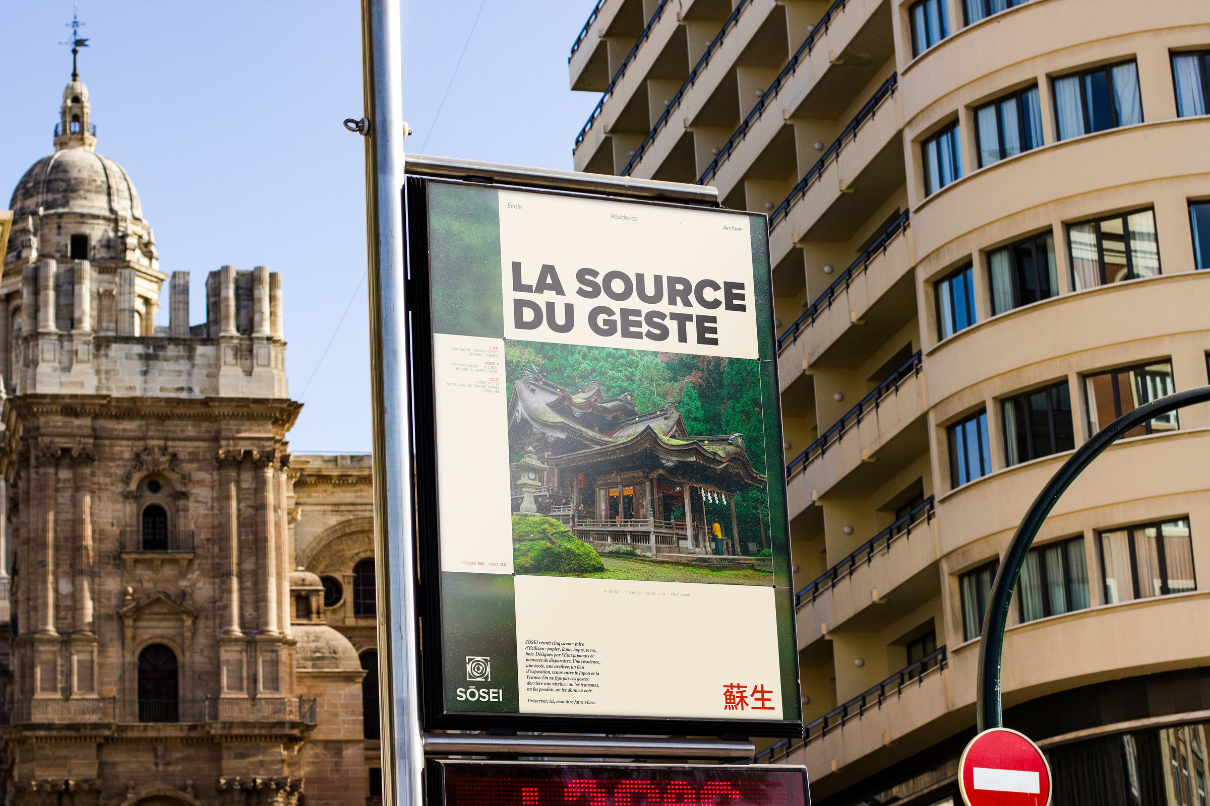 L'affiche « La source du geste » sur un panneau urbain, entre une église baroque et un immeuble