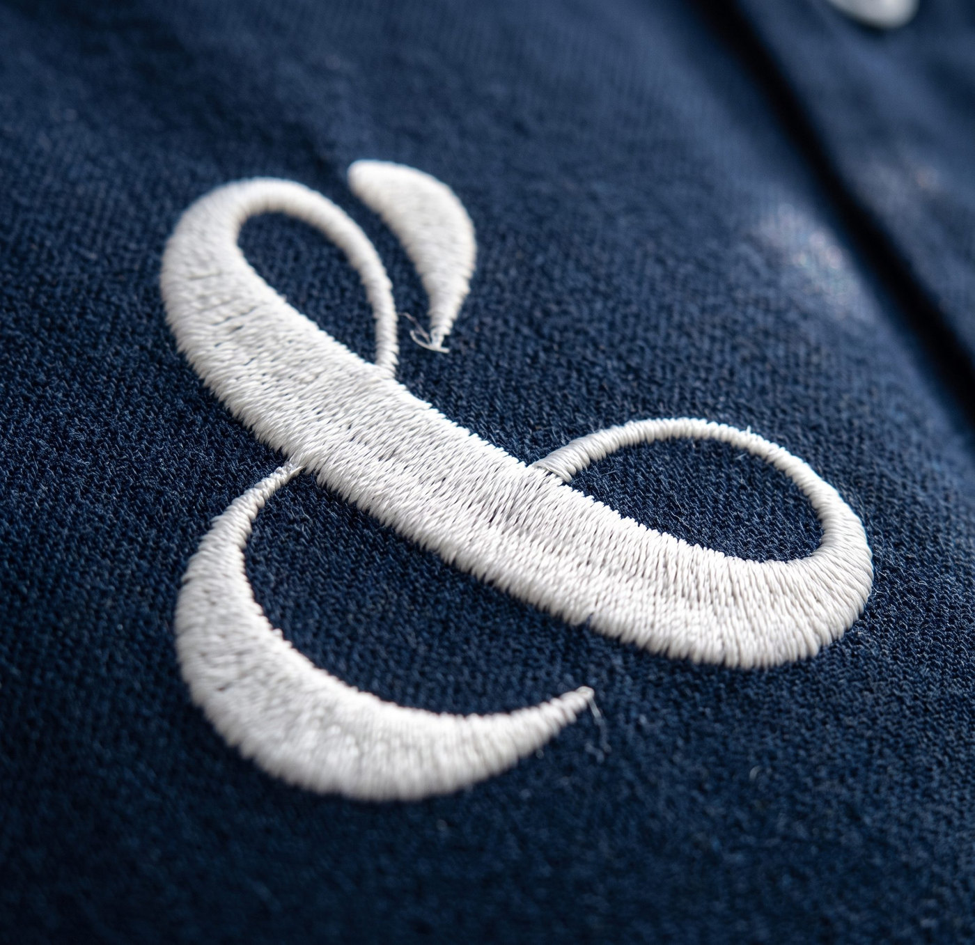 Une esperluette brodée en fil blanc sur une maille navy